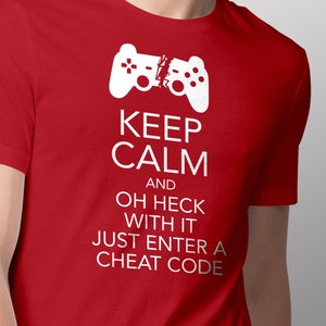 May include: Red t-shirt with a white graphic of a broken video game controller and the text "Keep Calm and Oh Heck With It Just Enter A Cheat Code".
