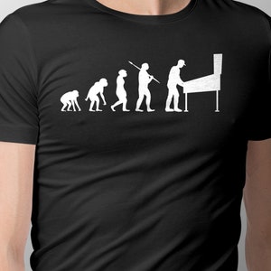 May include: A black t-shirt with a white graphic of the evolution of man, ending with a man playing a pinball machine.