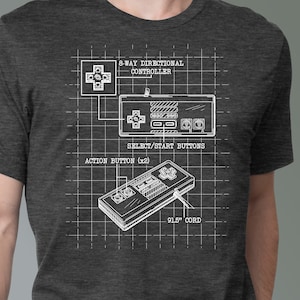 May include: A dark heather grey t-shirt with a white graphic of a vintage video game controller. The graphic includes a diagram of the controller's buttons and a 91.5 inch cord.