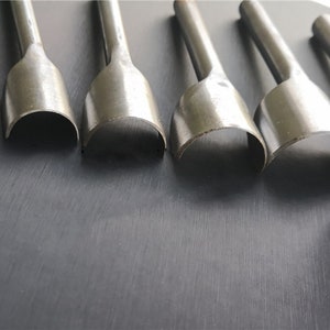 May include: Five silver metal leather hole punches of different sizes. The punches are arranged in a row from largest to smallest.
