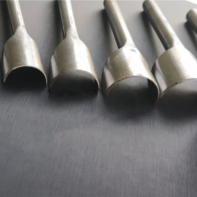 May include: Five silver metal leather hole punches of different sizes. The punches are arranged in a row from largest to smallest.