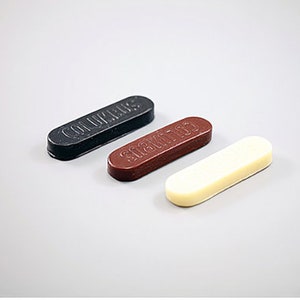 May include: Three sticks of sealing wax, one black, one brown, and one white. The black stick says "COLUMBUS" on it, the brown stick says "SCAMATO" on it, and the white stick has no text.
