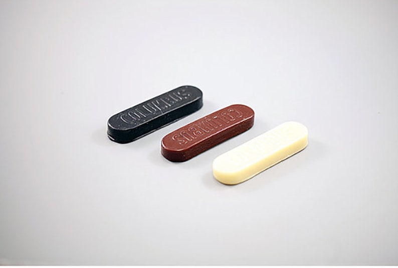 May include: Three sticks of sealing wax, one black, one brown, and one white. The black stick says "COLUMBUS" on it, the brown stick says "SCAMATO" on it, and the white stick has no text.
