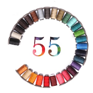 May include: A circle of 55 spools of thread in various colours, arranged in a rainbow pattern. The spools are on a white background.