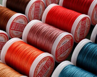 Op de afbeelding: Close-up van spoelen met gekleurd polyester garen, elk met het label "Ten Colors of Light" en "0.5mm".