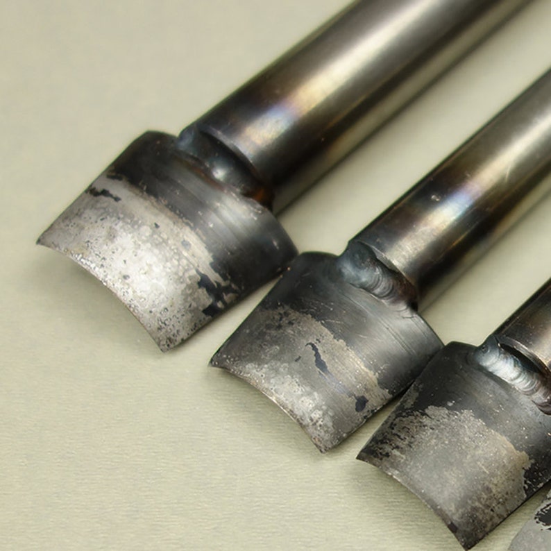 May include: Three metal leather crafting tools with rounded edges and a slightly curved shape. The tools are made of metal and have a silver finish.