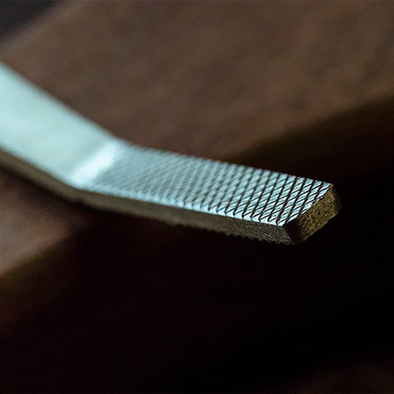 Peut inclure: Gros plan sur une lime en m&eacute;tal avec une surface &agrave; grain fin. La lime est de couleur argent&eacute;e et a une forme rectangulaire.