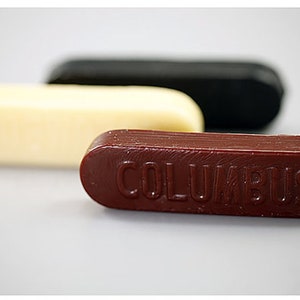 May include: Three sticks of shoe polish in different colors: white, black, and brown. The brown stick has the word "COLUMBUS" embossed on it.