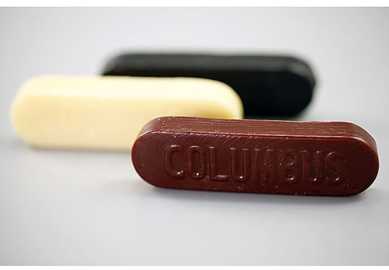May include: Three sticks of shoe polish in different colors: white, black, and brown. The brown stick has the word "COLUMBUS" embossed on it.
