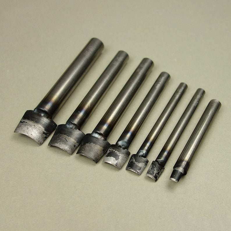 May include: Set of eight metal leather punches with different sized tips. The punches are silver in color and have a slightly worn look.