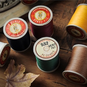 Pode incluir: Conjunto de carretéis de fio em várias cores, incluindo marrom, verde, vermelho, preto e amarelo. Cada carretel tem um rótulo com texto em francês e a marca "Lin Cable".