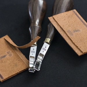 Puede incluir: Dos herramientas de trabajo de cuero con mangos de madera y cuchillas de metal. Las herramientas están etiquetadas como "Yorkshire Hand Made" y "6".