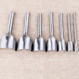 May include: Set of eight silver leather hole punches with rounded edges. The punches are arranged in a row from largest to smallest.
