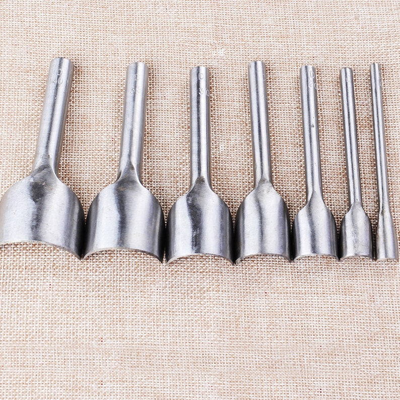 May include: Set of eight silver leather hole punches with rounded edges. The punches are arranged in a row from largest to smallest.
