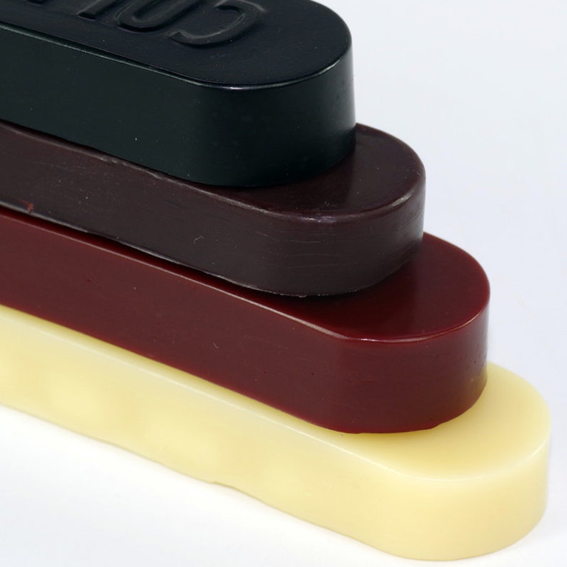 May include: Four bars of wax in different colors: black, dark red, light red, and cream. The bars are stacked on top of each other.