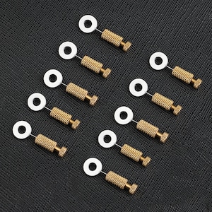 Puede incluir: Diez herramientas de metal de color dorado con cabezales circulares blancos. Las herramientas están dispuestas en una cuadrícula sobre una superficie negra texturizada.