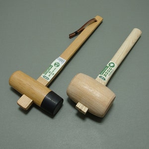 May include: Two wooden mallets with handles. The mallet on the left has a black rubber head and the mallet on the right has a natural wood head. Both mallets have labels that say "WOOD HAMMER".