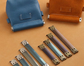 Könnte beinhalten: Zwei kleine Ledertaschen, eine blaue und eine orange, mit Metallverschlüssen. Sechs Metallschlaufen mit antikem Messingfinish.
