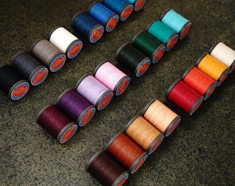 May include: Assortment of spools of thread in various colors, including red, orange, yellow, green, blue, purple, and white. The spools are arranged in a pattern on a dark gray surface.
