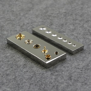 May include: Two polished metal display trays with a variety of round, gold-colored knobs and buttons. The knobs and buttons are arranged in a row on each tray.