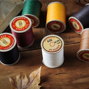 Pode incluir: Conjunto de seis rolos de fio em várias cores, incluindo preto, vermelho, verde, amarelo, branco e marrom. Os rolos são etiquetados com o texto "CABLE" e "AU CHINOIS".