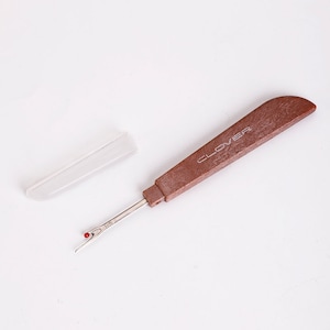 May include: A brown plastic thread cutter with a silver blade and a red tip. The cutter has a white plastic case and the word "CLOVER" printed on the handle.