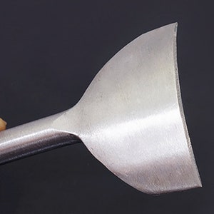 Puede incluir: Primer plano de una herramienta de marroquiner&iacute;a met&aacute;lica con una cuchilla curva. La herramienta tiene un acabado plateado pulido y un mango redondeado. La cuchilla es ancha y ligeramente curvada, dise&ntilde;ada para cortar y dar forma al cuero con precisi&oacute;n.