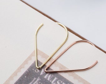 Puede incluir: Dos pendientes minimalistas, uno dorado y otro de oro rosa, en forma de lágrima. Los pendientes están sobre una superficie blanca.