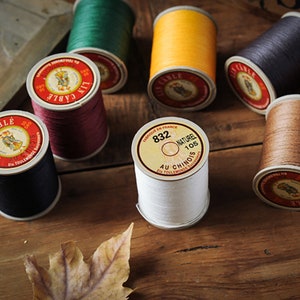 Puede incluir: Surtido de carretes de hilo en varios colores, incluyendo verde, amarillo, rojo, negro, marrón y blanco. Los carretes tienen etiquetas con texto en francés, incluyendo "Fabrique en France" y "Au Chinois".
