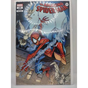 Puede incluir: Portada del cómic The Amazing Spider-Man #17. Spider-Man con un traje rojo y azul se balancea de una telaraña. La portada presenta un fondo de paisaje urbano con pájaros blancos y el logo de Marvel.