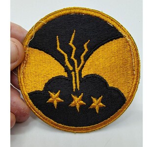 May include: Embroidered patch with a circular design. The patch features a black background with three gold stars at the bottom and a stylized gold lightning bolt design. The outer border is gold.