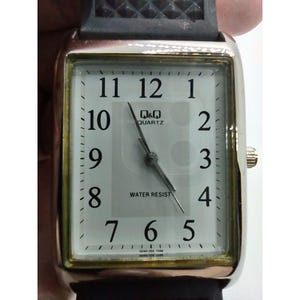May include: Silver rectangular watch with a white face, black numerals, and black hands. The watch face displays "Q&Q QUARTZ" and "WATER RESIST". The watch has a black strap.