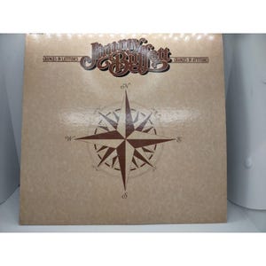 Pode incluir: Uma capa de álbum de vinil vintage com uma rosa dos ventos e o texto "Jimmy Buffett Changes in Latitudes Changes in Attitudes".