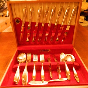 Puede incluir: Una caja de madera con un interior de terciopelo rojo que contiene un juego de cubiertos de plata. Los cubiertos incluyen cuchillos, tenedores y cucharas.