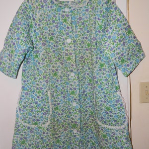 May include: A white quilted robe with a floral print in shades of blue, green, and purple. The robe has a collar, long sleeves, and a button-up front. It features lace trim around the collar and pockets.