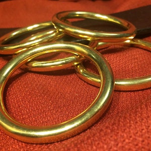 Puede incluir: Cinco anillos de metal de color dorado apilados uno encima del otro. Los anillos son lisos y brillantes.