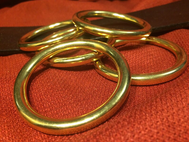 Puede incluir: Cinco anillos de metal de color dorado apilados uno encima del otro. Los anillos son lisos y brillantes.
