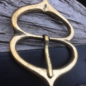 Pode incluir: Uma fivela de cinto de metal dourado com um design &uacute;nico e ornamentado. A fivela tem duas al&ccedil;as e uma parte superior pontiaguda.