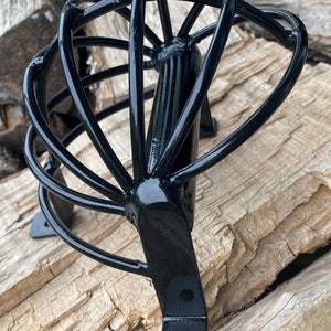 May include: Black metal bike rack with a curved design and multiple bars. The rack is mounted to a wooden surface.