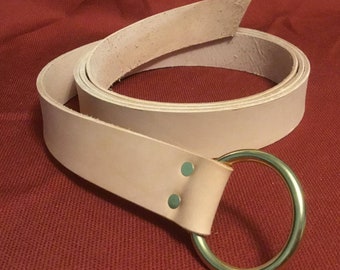 Peut inclure: Une ceinture en cuir marron clair avec une boucle en laiton en forme d'anneau. La ceinture est enroulée et la boucle est sur le côté droit de l'image.