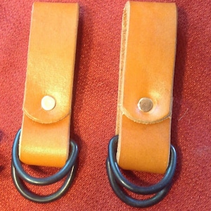 May include: Two brown leather belt loops with black metal double D-rings. The loops have a small flap with a silver rivet.
