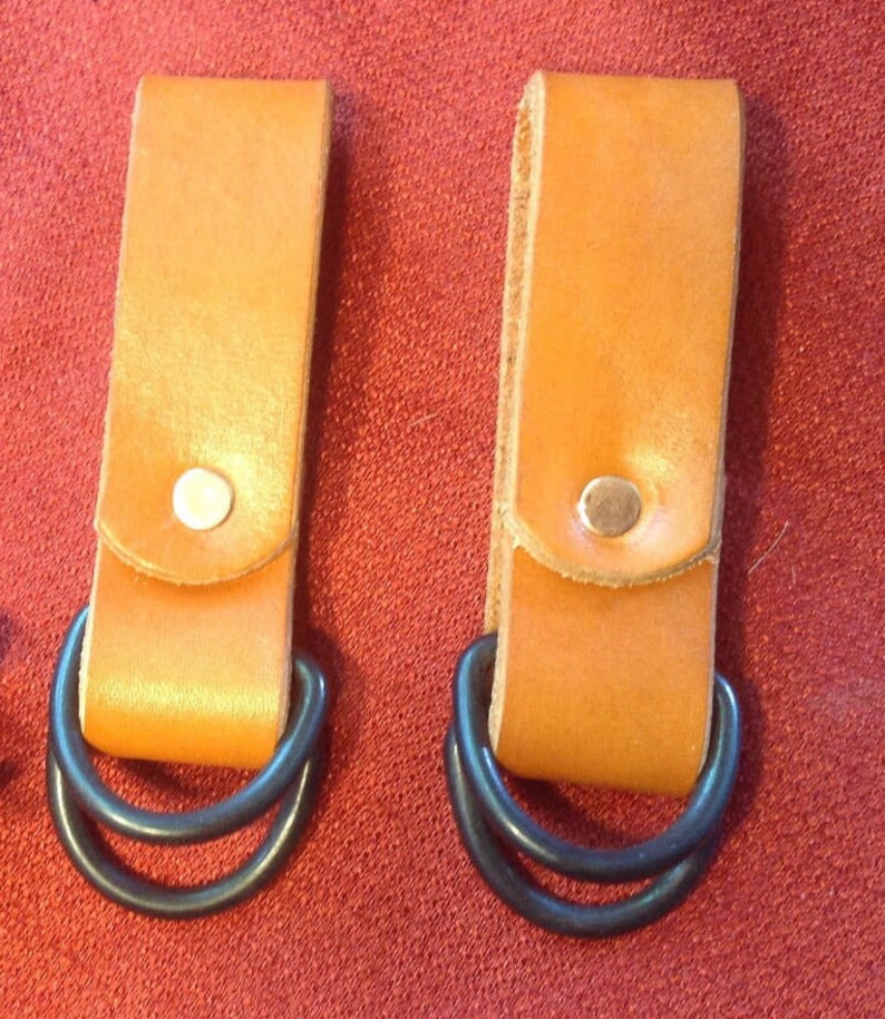 May include: Two brown leather belt loops with black metal double D-rings. The loops have a small flap with a silver rivet.