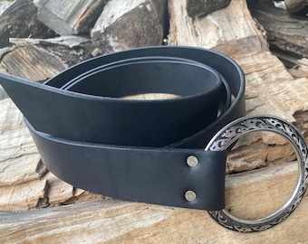 May include: A black leather belt with a large, silver, ornate, circular buckle. The buckle has a detailed design of swirling lines and shapes.