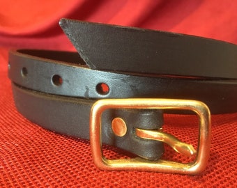 May include: A black leather belt with a rectangular gold-colored buckle. The belt has several evenly spaced holes and a pointed end. The buckle is a simple, classic design. The belt is shown against a red background.