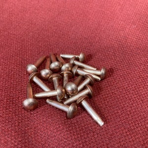 Puede incluir: Un mont&oacute;n de remaches de metal de color plateado con cabezas redondeadas. Los remaches est&aacute;n dispuestos en un patr&oacute;n aleatorio sobre una superficie de tela roja.
