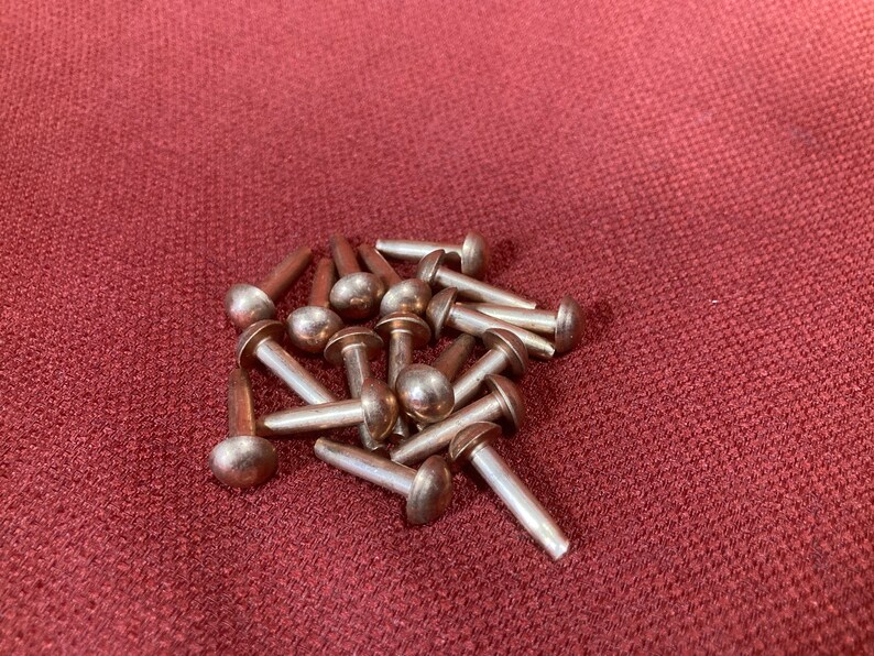Puede incluir: Un mont&oacute;n de remaches de metal de color plateado con cabezas redondeadas. Los remaches est&aacute;n dispuestos en un patr&oacute;n aleatorio sobre una superficie de tela roja.