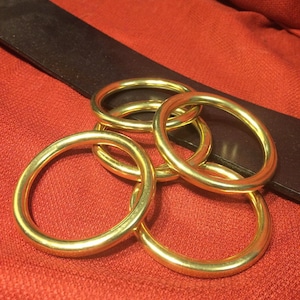 Puede incluir: Cinco anillos de metal de color dorado entrelazados. Los anillos est&aacute;n sobre una superficie de tela roja.