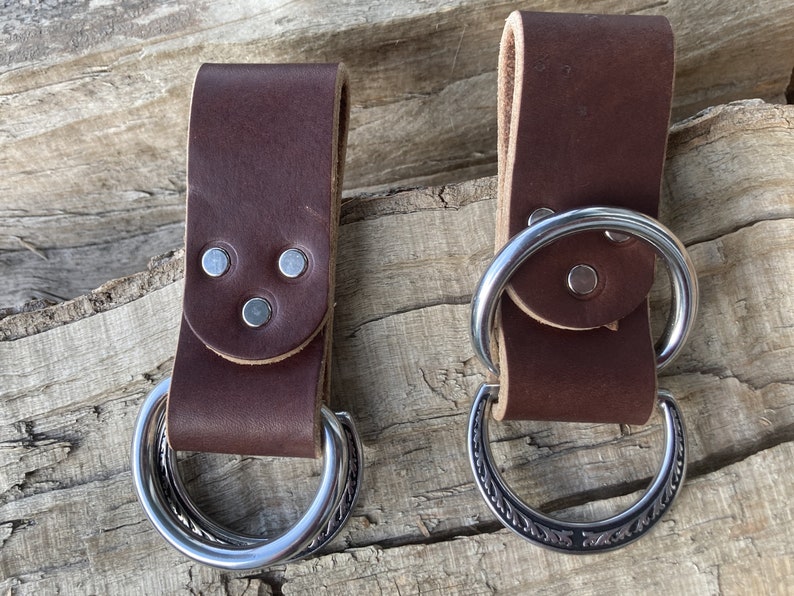 May include: Two brown leather belt loops with metal rings. One ring is plain and the other has a decorative design.