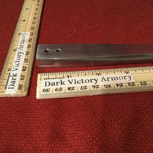Puede incluir: Una barra de metal plateado con dos agujeros perforados. La barra mide aproximadamente 7,6 cm de largo y est&aacute; sobre una superficie roja. La barra est&aacute; etiquetada como "Dark Victory Armory".