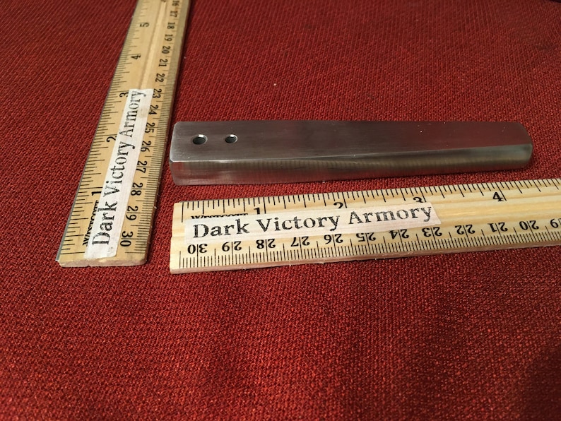 Puede incluir: Una barra de metal plateado con dos agujeros perforados. La barra mide aproximadamente 7,6 cm de largo y est&aacute; sobre una superficie roja. La barra est&aacute; etiquetada como "Dark Victory Armory".